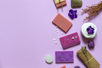 Layout of purple eco soap,natural pumice, washcloth and flowers . Top view on a lilac background with space