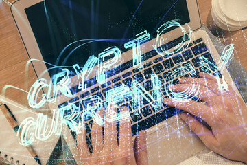 Double exposure of man's hands typing over computer keyboard and crypto currency theme hologram...