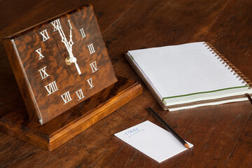 Artisanal wooden clock on the table, with paper to notations and pencil - 01:00 o'clock
