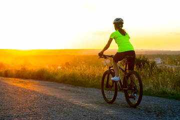 Beautiful girl cyclist riding a bike on the road towards the sunset. Nature and recreation. Hobbies and sports