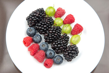 berries raspberries, blueberries, gooseberries and blackberries on a white plate. useful vitamin healthy food fruit. healthy vegetable breakfast
