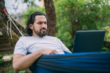 Obraz premium A man works with a laptop in a hammock in a country house