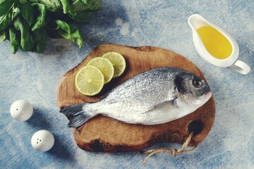 Fresh uncooked dorado with lime, salt and pepper on an olive board.