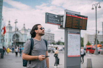 A man looks at the phone at the train schedule at the station