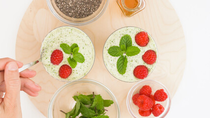 Celery banana smoothie with Chia seeds and honey in glasses, served with fresh raspberries and mint leaves, close up on kitchen table. Healthy breakfast, dessert, green detox smoothie recipe