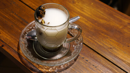 A glass of hot ginger milk on a wooden table. A special drink from Indonesia, pure milk mixed with grilled ginger