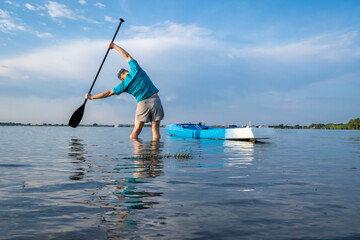 senior paddler is stretching and warming up before morning workout on a stand up paddleboard - Boyd Lake State Park in northern Colorado