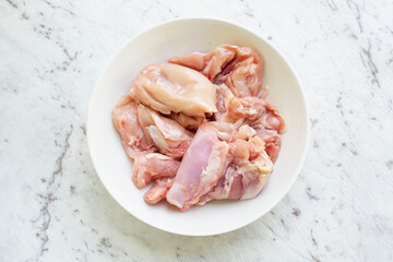 Raw chicken thighs in a bowl on a white marble background