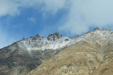 Rock formations on a mountain peak jut into a blue sky with faint clouds. The slopes of the...