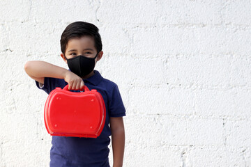 6-year-old boy with protective mask, lunch box and colors for back to school, new normal covid-19