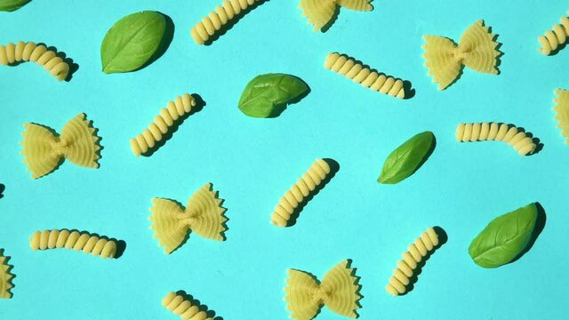 Uncooked curly pasta and basil leaf pattern on blue background. Traditional dry raw macaroni pattern. Nobody