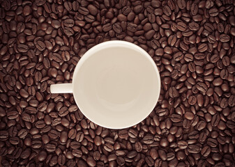 Roasted coffee bean background with white ceramic mug in the middle.