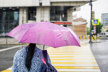 Woman with a pink umbrella in rainy weather crossing the pedestrian. Bad weather. Rainy day. Umbrella with raindrops. City street style.