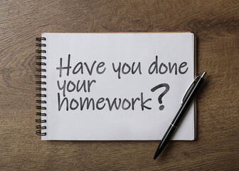 Pen and stylish notebook with phrase HAVE YOU DONE YOUR HOMEWORK? on wooden table, top view
