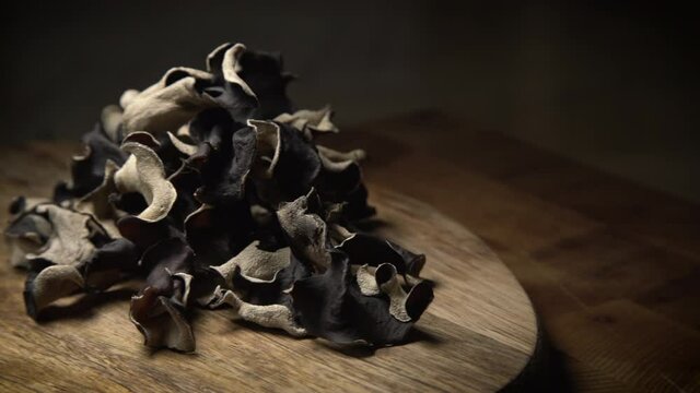 Close up shot of rotating dry black sliced mushroom on wooden background. Edible dark fungus - auricularia polytricha. Nobody