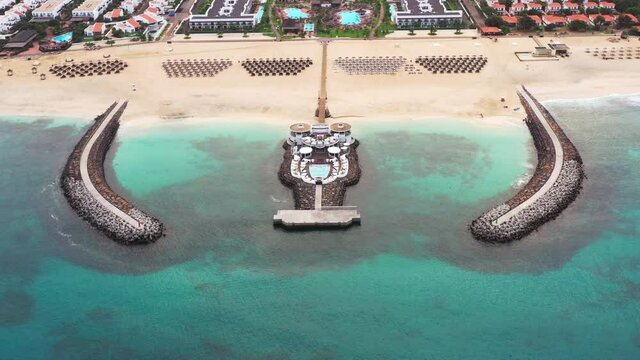 Aerial shot of a wide sandy beach tourist resort with a twin breakwater construction, sunbeds and umbrellas. Sal island, Cabo Verde