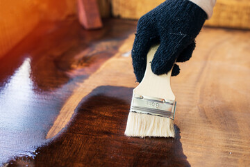 Hands with a brush to apply a protective lacquer to the wooden surface.brush paint clear lacquer on...