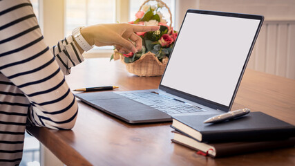 The hand of a woman pointing at the laptop screen on the table.