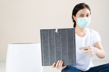 Asian woman wearing a hygiene protective face mask during changing a dirty air filter in the air...
