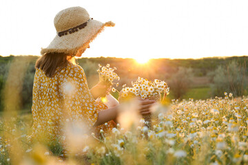 Woman with straw hat and handbag full of chamomiles resting in meadow
