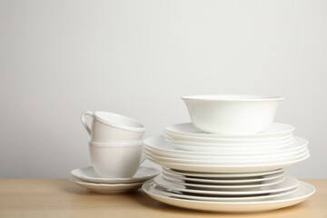 Clean plates, bowl and cups on wooden table against white background. Space for text