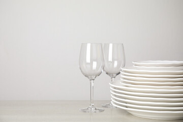 Stack of clean plates and glasses on table against white background. Space for text
