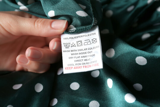 Woman reading clothing label with care instructions and content information on green polka dot garment, closeup