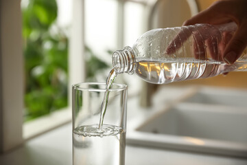 Woman pouring water from bottle into glass in kitchen, closeup