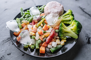 Plate of frozen vegetables and a meat cutlet on a gray table. Concept of saving time on cooking dinner and convenient storage of ready made frozen dishes