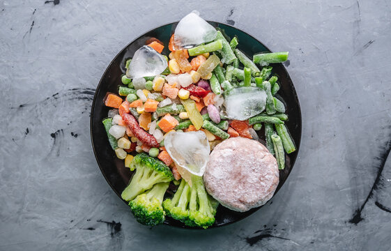 Plate of frozen vegetables and a meat cutlet on a gray table. Concept of saving time on cooking dinner and convenient storage of ready made frozen dishes