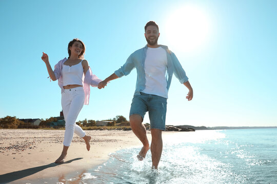 Happy young couple running on beach near sea, low angle view. Honeymoon trip - Powered by Adobe