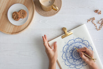 Female hands close up draw Decorative round floral mandala. Hobby and home relaxation. A mug of...