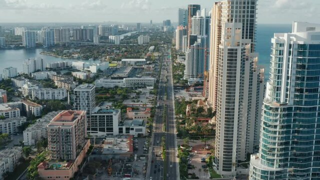 Miami city scenic skyline. Amazing straight shot of the Collins Avenue with the frontline modern apartment buildings with beautiful ocean view at sunset. Beach city aerial footage, vacation 4K aerial