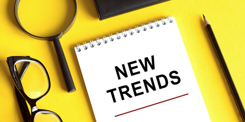 New Trends text written on notebook with glasses, magnifier end pen. Main trend of changing something. Popular and relevant topics. New trends in business. Recent and latest trend. Evaluation methods.