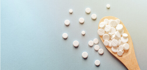 Close-up white pills, tablets in wooden spoon on blue table in the rays of sunlight . Medicine and health concept. pharmaceutics. Top view. Pills and vitamins