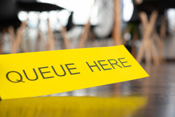 The image of a yellow sign to the queue here, attached to the floor, keeping distance