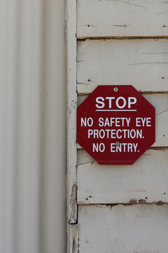 Red And White Sign Warning, Stop, No Safety Eye Protection, No Entry On The Exterior Of A Weathered Workplace Building