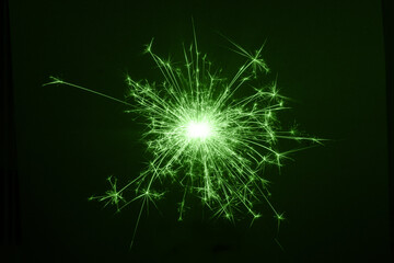 Festive New Year's single green sparkling burning sparkler or salute on a black background. Holiday concept, copy space.