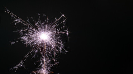 Christmas and New Year party sparkler on black burning colored sparkler on a black background, copy space