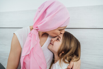 Cancer mother with a pink headscarf gives her blonde daughter a tender kiss