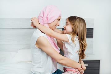 cancer mother with a pink headscarf happily hugging her blonde daughter
