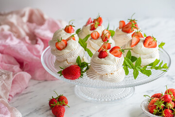 Mini Pavlova meringue nests with whipped cream and fresh strawberries on a glass cake stand