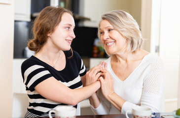 Happy senior woman chatting with young friend and at drinking tea home