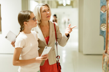 Fototapeta Intelligent female tutor helping tweenage girl exploring art pieces in art museum obraz