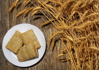 three wrapped pancakes on a white plate on a wooden table against a background of wheat ears