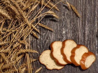 Sliced ​​white wheat bread and ears of wheat lie on a wooden table