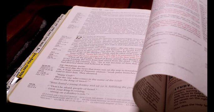 4K clip of Bible on wooden table open to Gospel of John, moving over while page is being turned. You can see some highlighted and underlined verses.