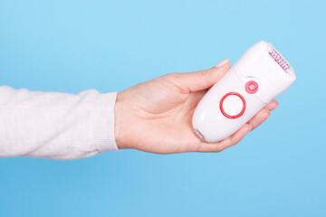 Hand with white electric epilator. Isolated on blue background.