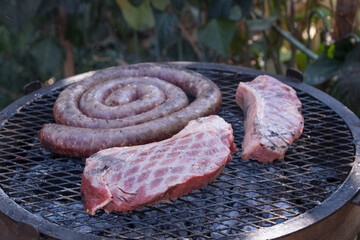 Steak and sausage cooking on a grid outdoors on a barbecue fire image in horizontal format