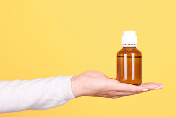 Hand with medicine bottle, chemistry container. Isolated on yellow background.